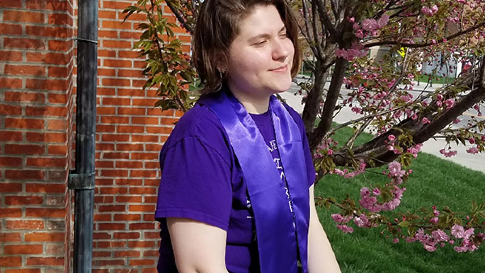 Photograph of Kyla sitting on a ledge with her sorority graduation stoles 