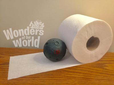 Photo of a roll of toilet paper with a few pieces rolled out. A moon stress ball is on top of one of the rolled out toilet paper pieces.