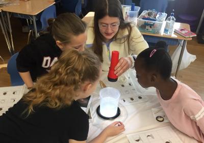 Photograph of Kate holding up a flashlight and flashing light down on a beaker of a spiral galaxy that was created with baking soda and water