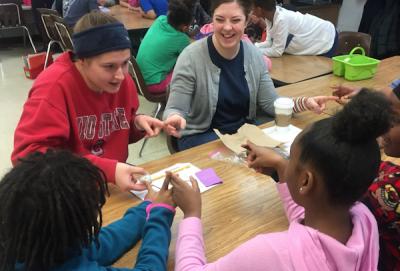 Photograph of Kate with 4th graders touching fingers to making a circuit to get an energy ball to light up