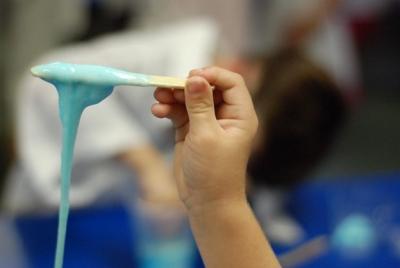 Photograph of a kid holding up a popsicle stick with homemade blue slime on it