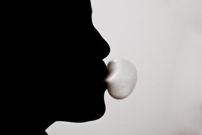 Photo of a shadowed person blowing a bubble with chewing gum