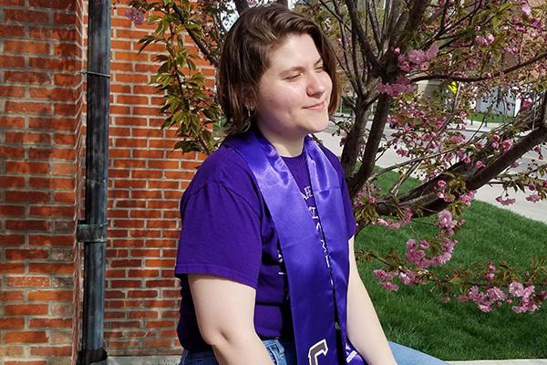 Photograph of Kyla sitting on a ledge with her sorority graduation stoles