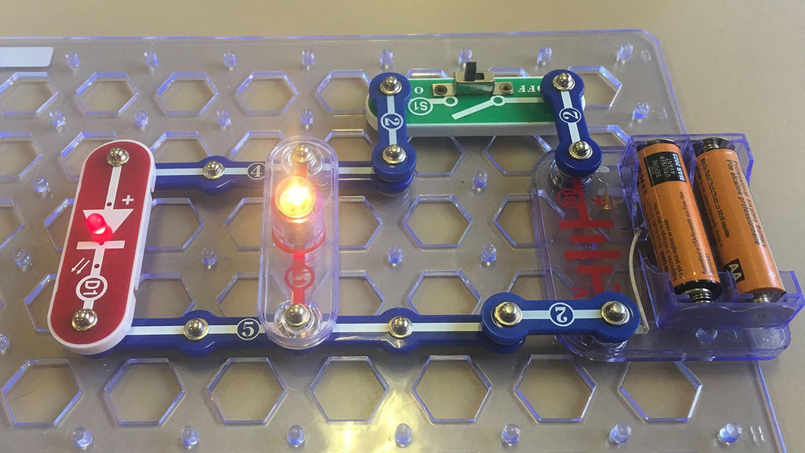 Photograph of a closed parallel circuit created using snap circuits, an LED diode, light bulb, switch, and batteries. 